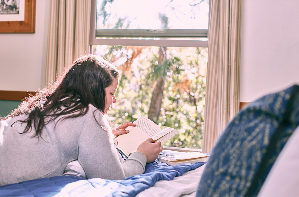 Woman reading a book in a guest room at Rush Creek Lodge at Yosemite.